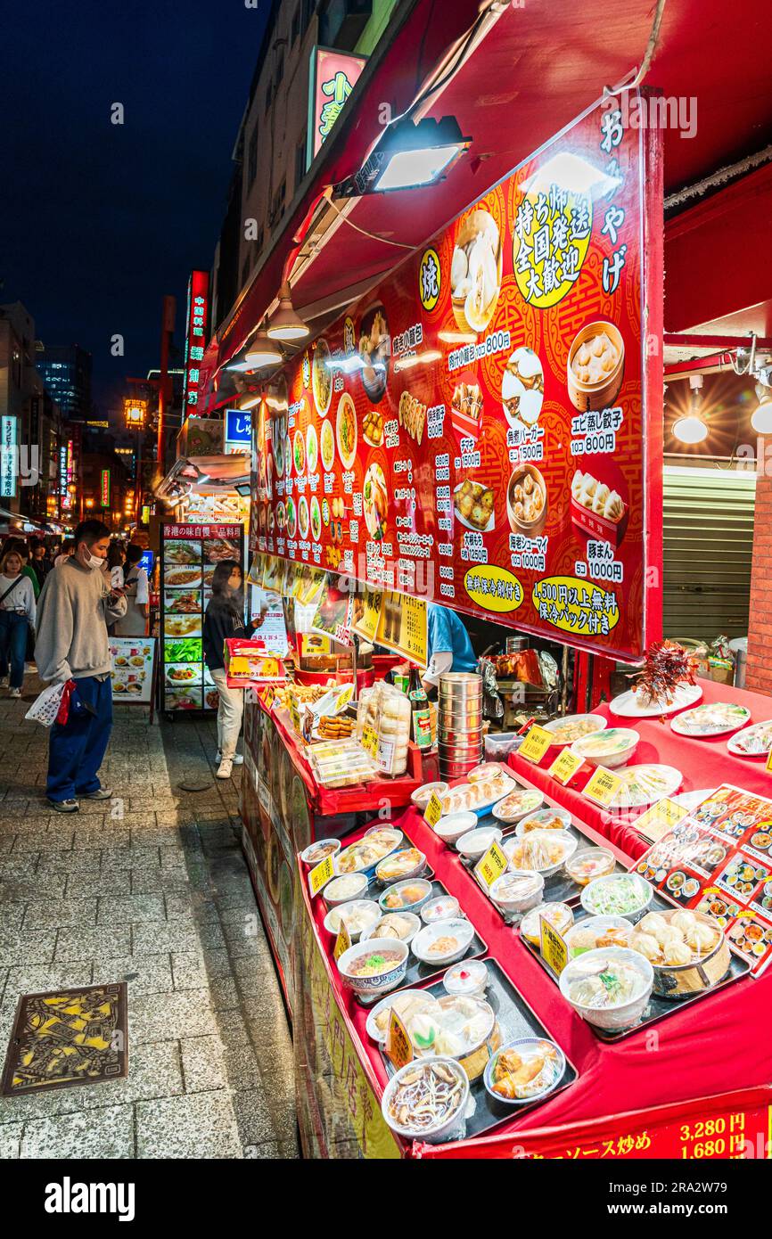 Rangée de plats chinois avec assiettes de divers aliments tels que des boulettes et du curry avec des cartes de menu suspendues au-dessus. Chinatown la nuit, Kobe. Banque D'Images