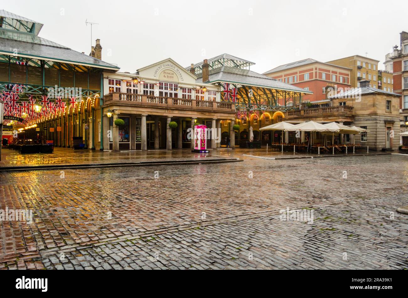 Le populaire marché de Covent Garden de Londres par jour de pluie avec Union Jack, drapeaux britanniques accrochés au-dessus des magasins. La cabine téléphonique Love est un site rare à Londres Banque D'Images