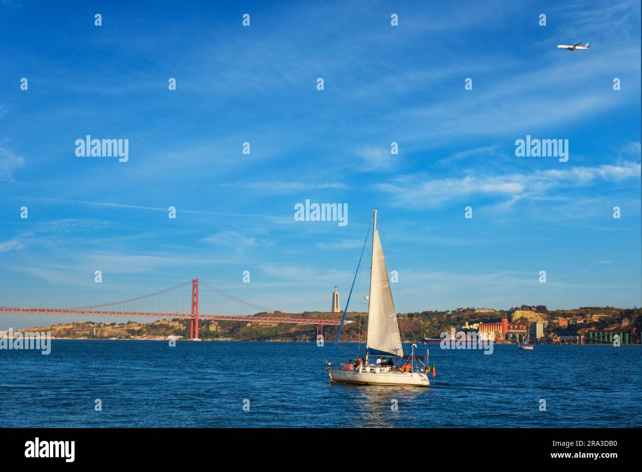 Vue sur le pont 25 de Abril au-dessus du Tage, le monument Christ le Roi et un yacht au coucher du soleil. Lisbonne, Portugal Banque D'Images