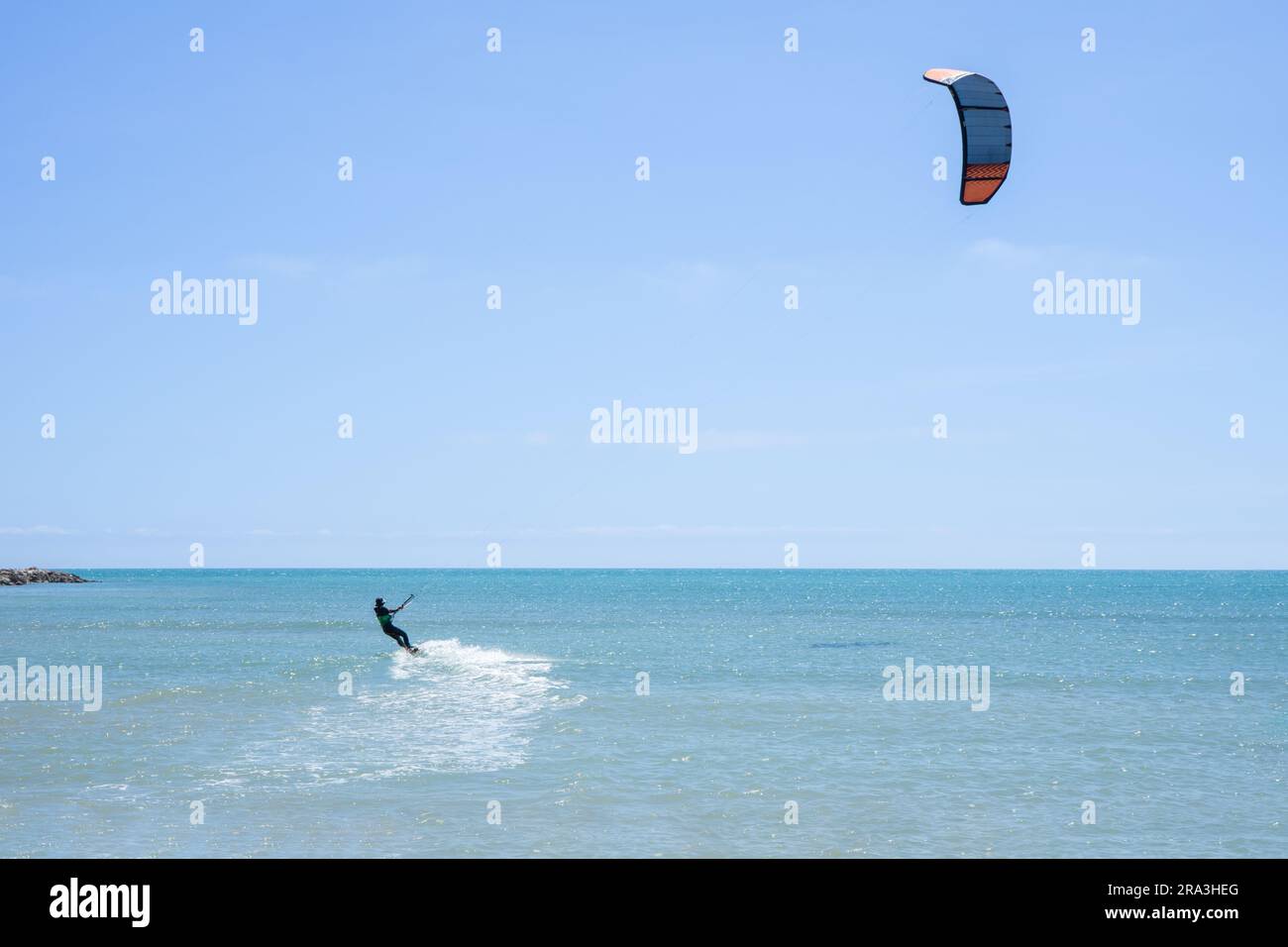 Vue arrière d'un kitesurfer à cheval sur son cerf-volant dans une mer calme. Sports nautiques Banque D'Images