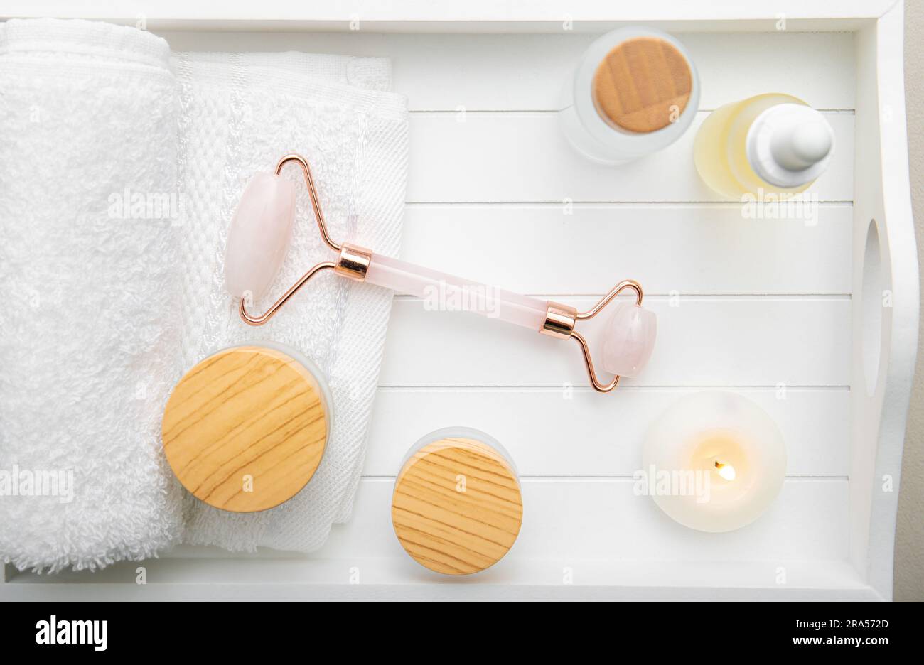 Outil de roulement du visage en pierre de quartz rose, divers produits génériques de soins de la peau du visage et du corps crèmes hydratantes huiles sur plateau en bois blanc Lumière de studio. Banque D'Images