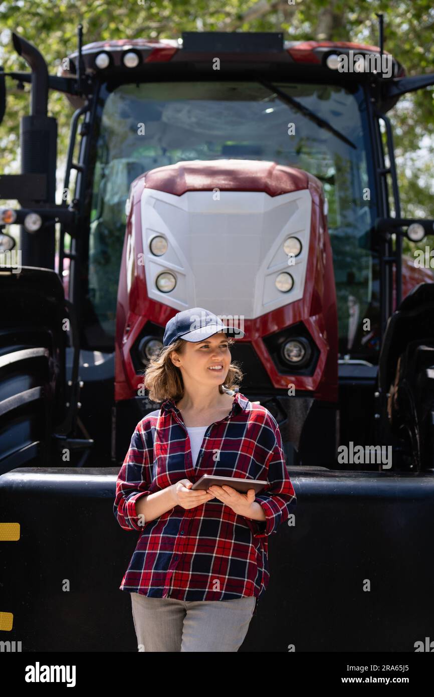 Femme agriculteur avec une tablette numérique sur le fond d'un tracteur agricole. Banque D'Images