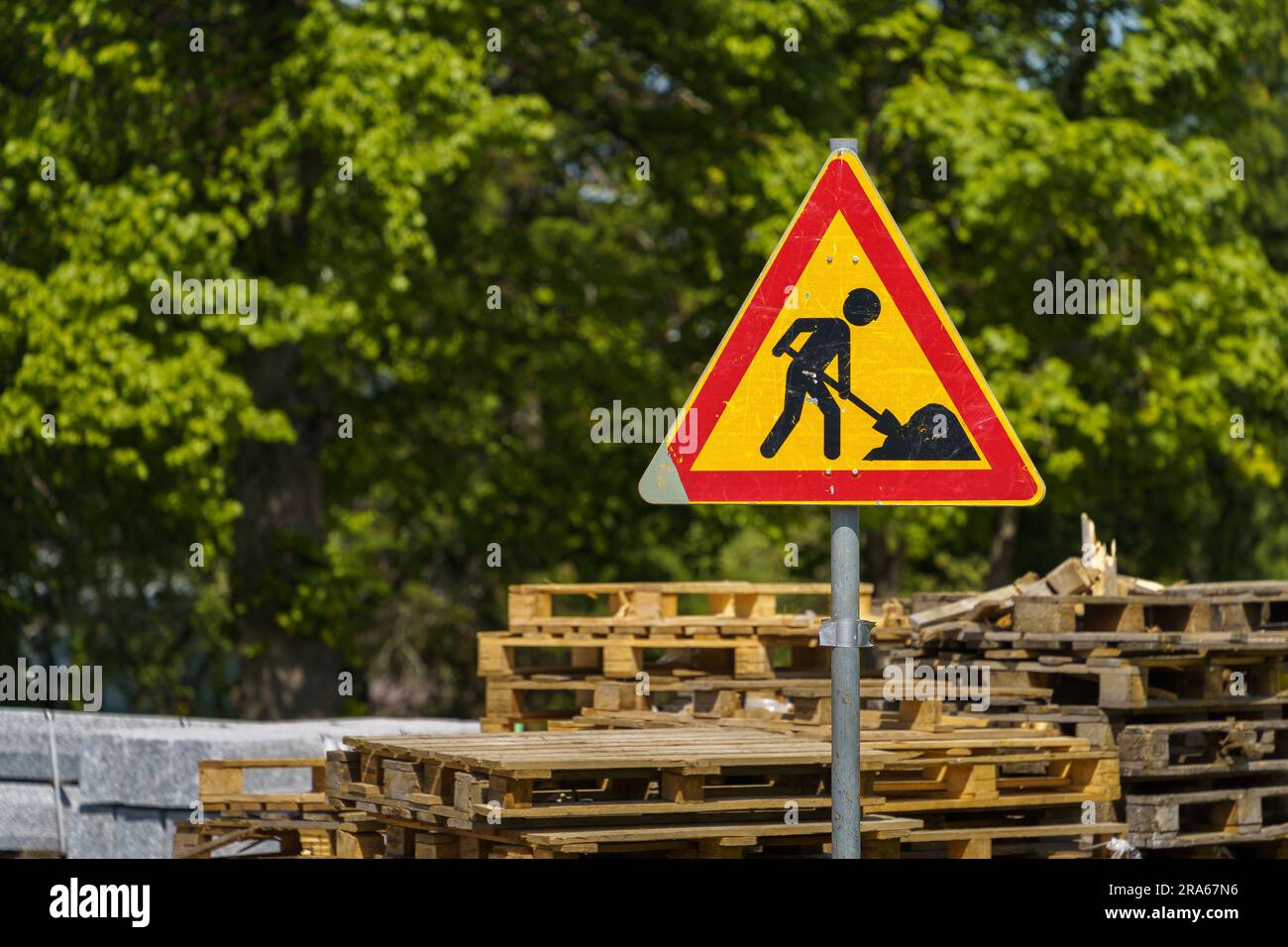 Panneau d'avertissement de travaux routiers en été avec des palettes en bois en arrière-plan. Banque D'Images