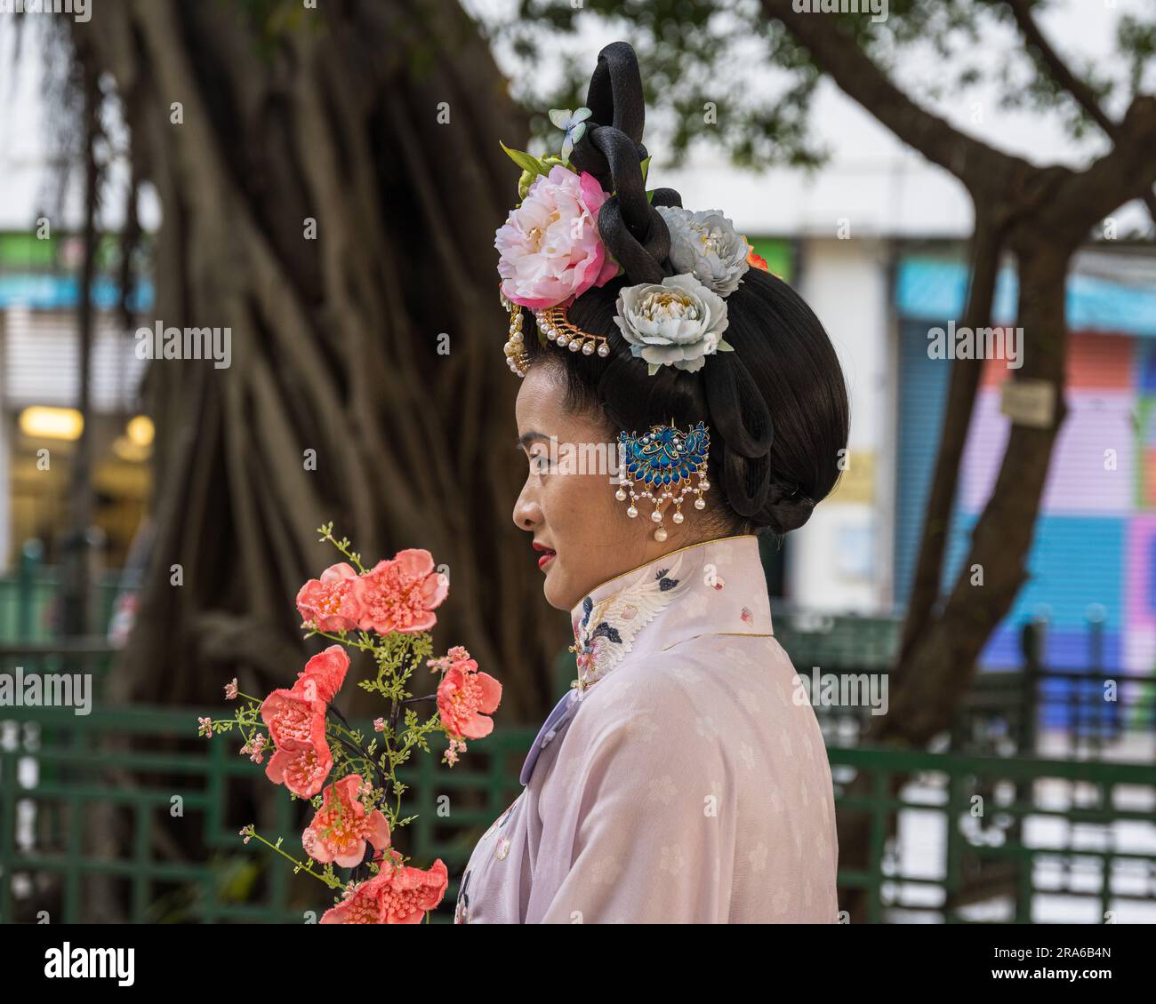 Hong Kong, Chine -- 11 mars 2023. Une femme chinoise vêtue d'une robe de mariage rose tient des fleurs roses. Banque D'Images