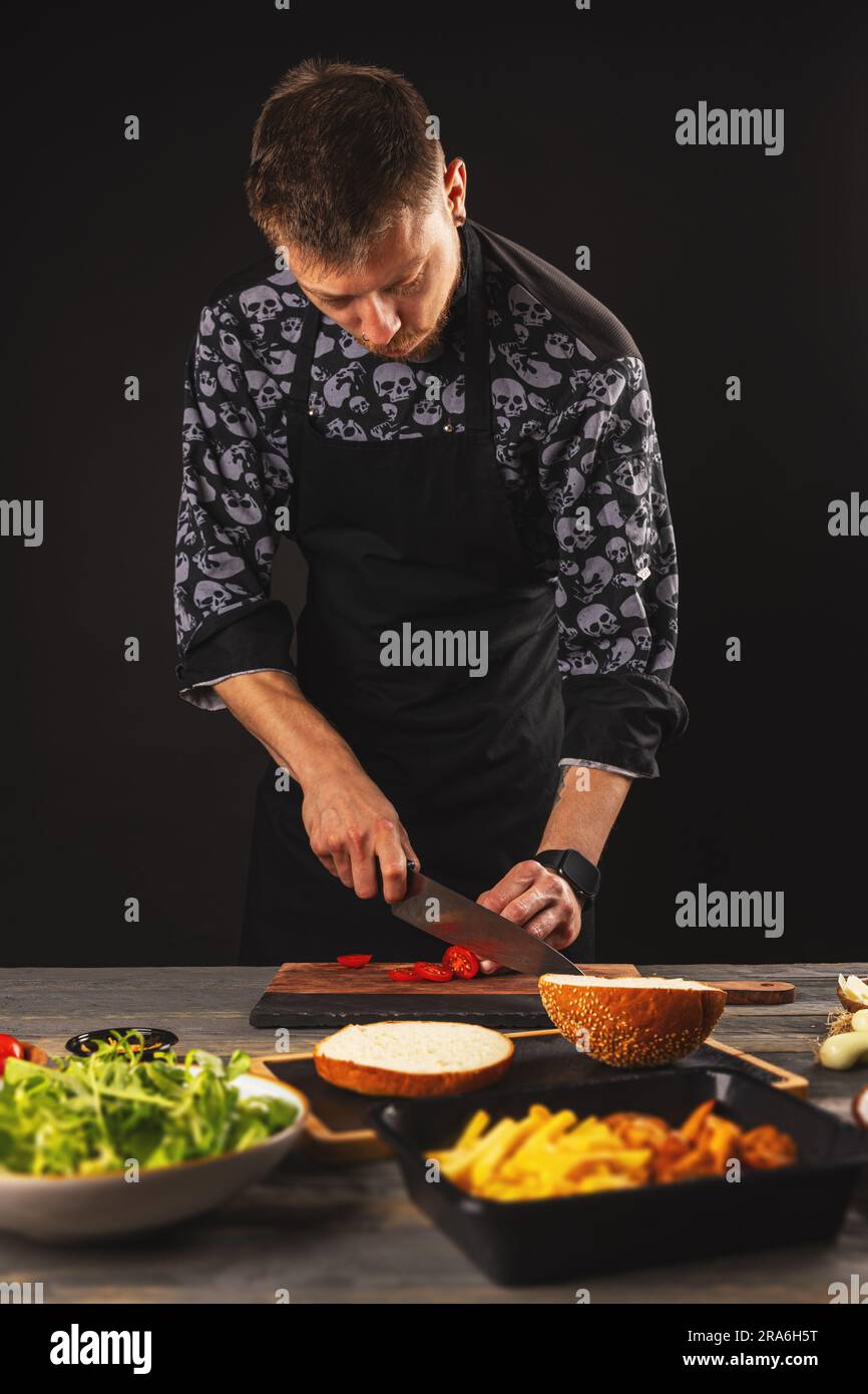 Chef en tranches de tomates pour hamburgers. Le processus de fabrication d'un hamburger. Banque D'Images