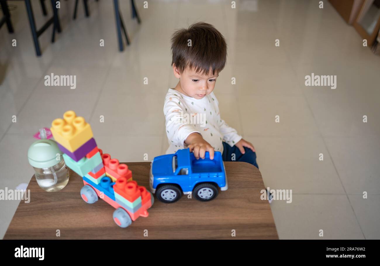 Un bébé d'un an et demi de course mixte jouant avec des blocs de construction colorés et un véhicule de jeu empilable en forme. Tout-petit assis près d'un café Banque D'Images