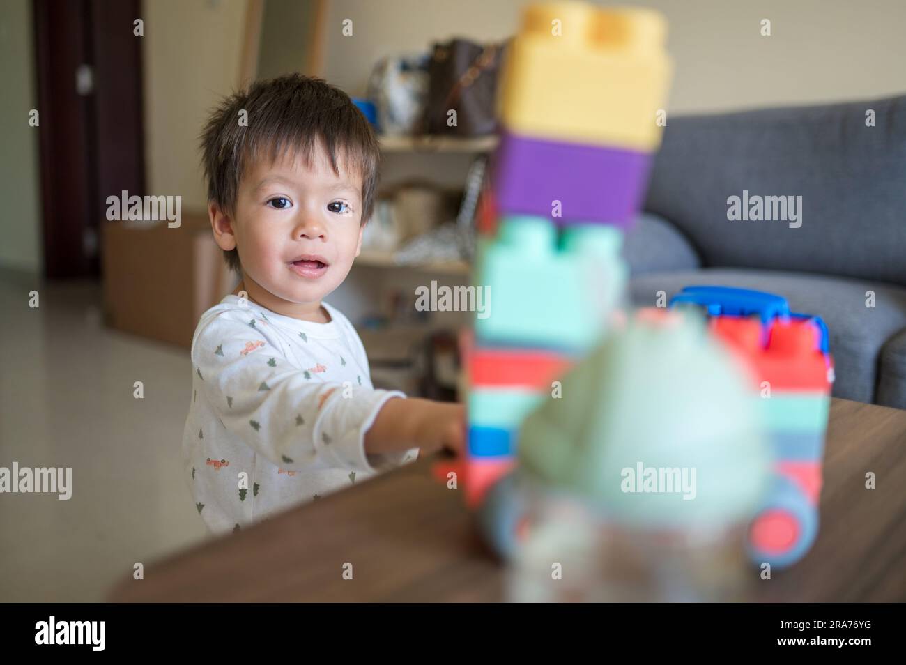 Un bébé d'un an et demi de course mixte jouant avec des blocs de construction colorés et un véhicule de jeu empilable en forme. Tout-petit assis près d'un café Banque D'Images