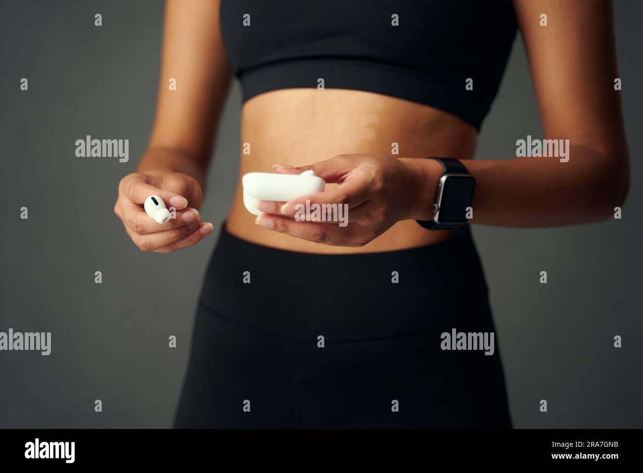 Gros plan d'une jeune femme biraciale portant un appareil de suivi de fitness tenant des écouteurs intra-auriculaires sans fil Banque D'Images