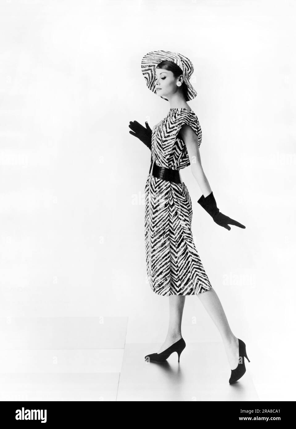 États-Unis: c. 1964 Une femme portant une robe de jour en coton à zébrée imprimée et un chapeau de slouch assorti conçu par Estevez Banque D'Images