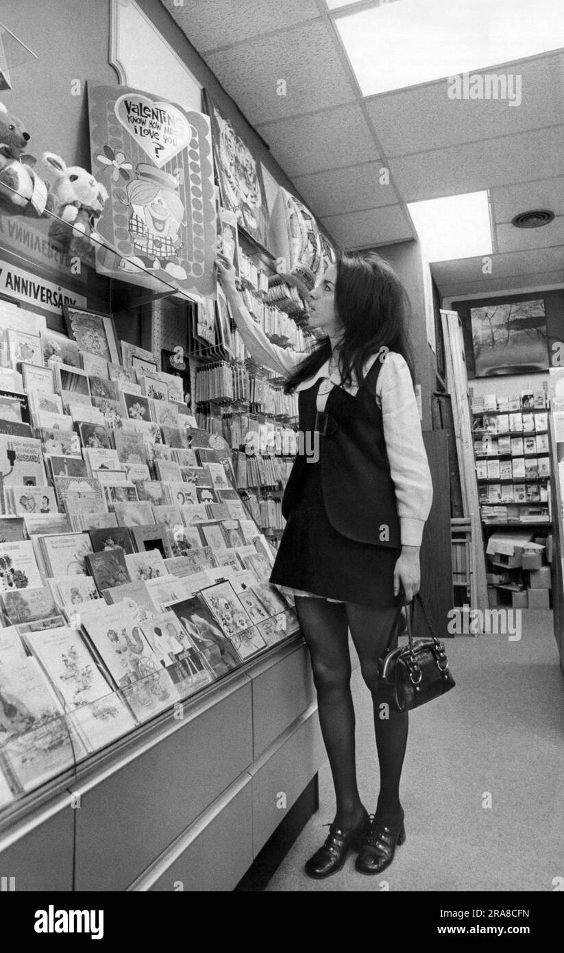 New York, New York: 12 février 1971 Une jeune femme portant une mini jupe va faire du shopping pour les cartes de Saint-Valentin surdimensionnées. Banque D'Images