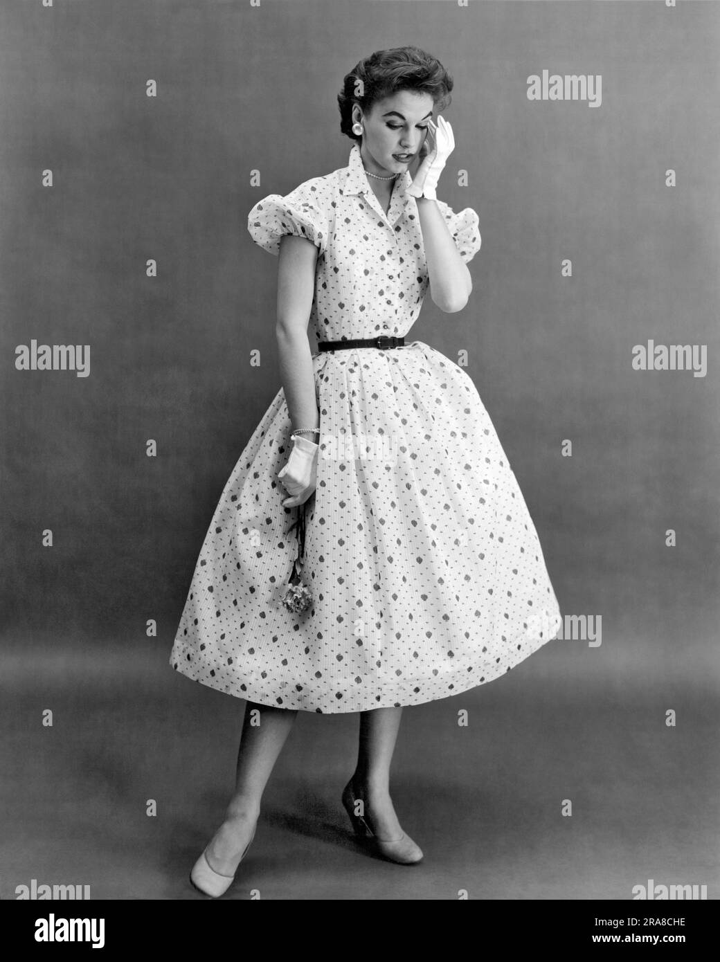 États-Unis: c. 1956 Une femme qui modélise une robe à l'imprimé de fraise succulente sur une faible fossité avec de petites manches bouffantes pour donner à cette 'petite fille' look qui est si tendance aujourd'hui. La Maker Nali-Bee ajoute également une touche de paillettes avec des boutons en strass. Banque D'Images