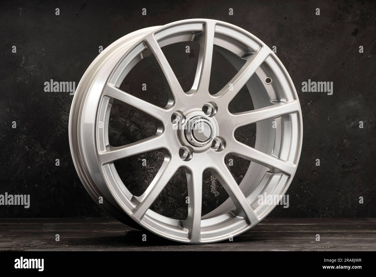 roues en alliage d'argent pièces automobiles légères avec de nombreuses branches sur un fond texturé foncé. Banque D'Images