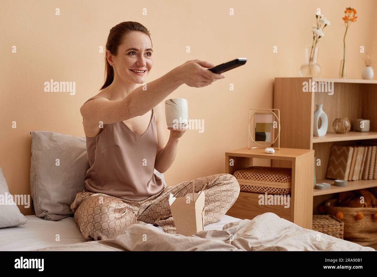 Portrait d'une jeune femme heureuse tenant la télécommande et regardant la télévision en profitant d'un week-end confortable à la maison, espace de copie Banque D'Images