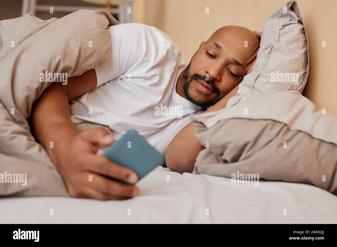 Portrait d'un homme noir adulte allongé au lit à la maison et à l'aide des réseaux sociaux défilants de smartphone Banque D'Images