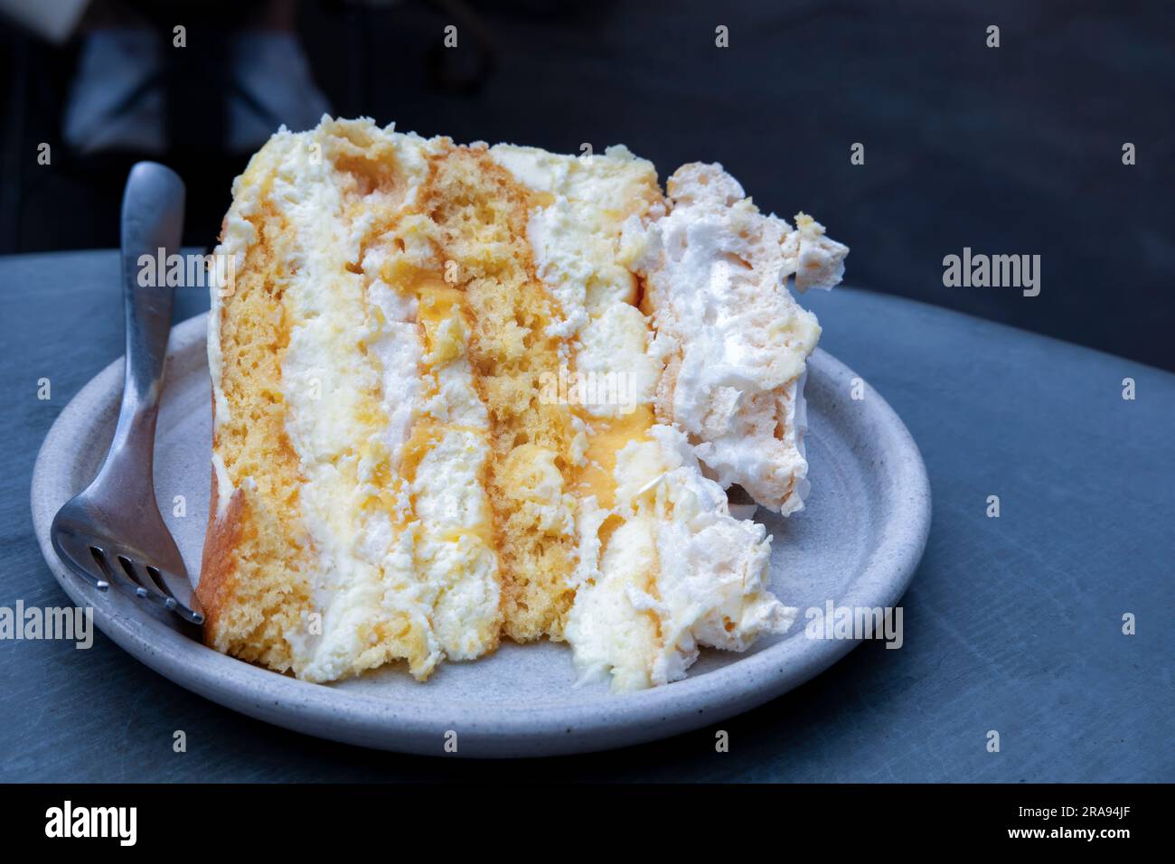 Une seule portion plaquée d'un gâteau de meringue au citron fait maison servi à une table plaquée. le gâteau a une garniture au citron caillé et un glaçage à la crème au beurre Banque D'Images