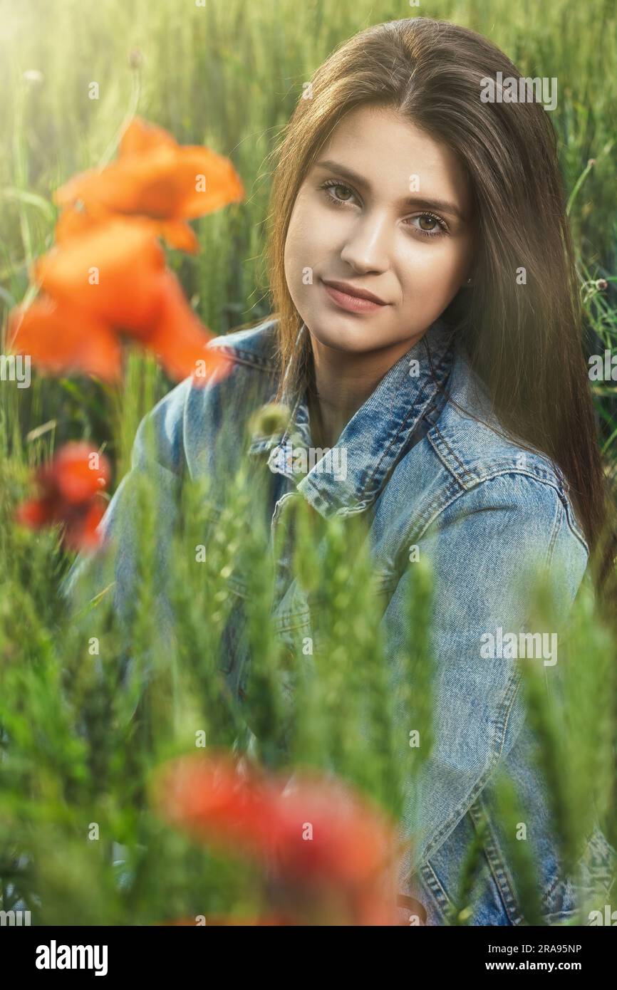Gros plan portrait d'une belle fille bronzée à cheveux longs brune vêtue de jeans assis dans un cornfield. Verticalement. Banque D'Images