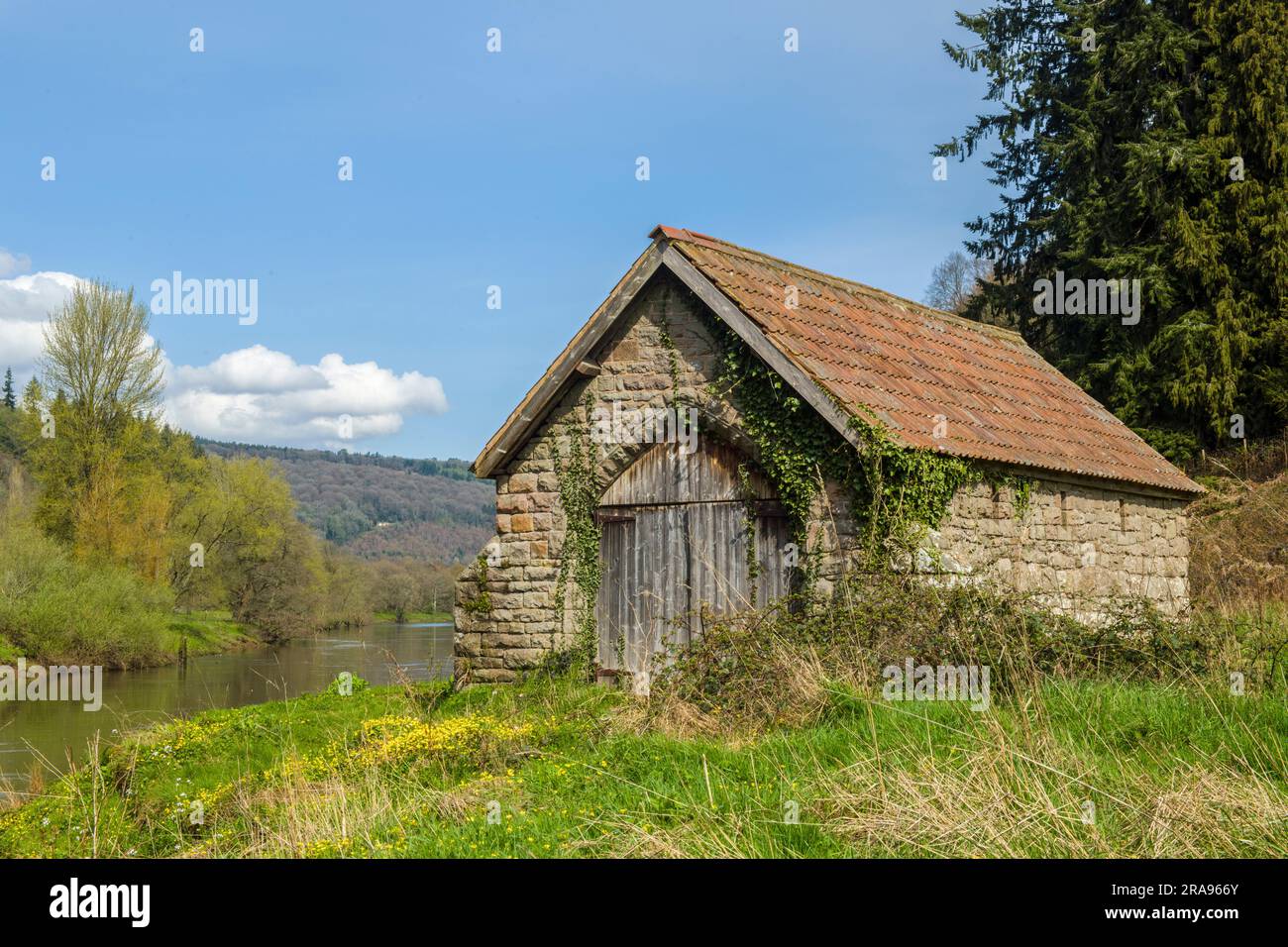 Un hangar à bateaux construit en pierre et tuile avec une porte d'accès en bois sur le côté Gloucestershire de la rivière Wye juste à côté du sentier menant de Brockweir Banque D'Images
