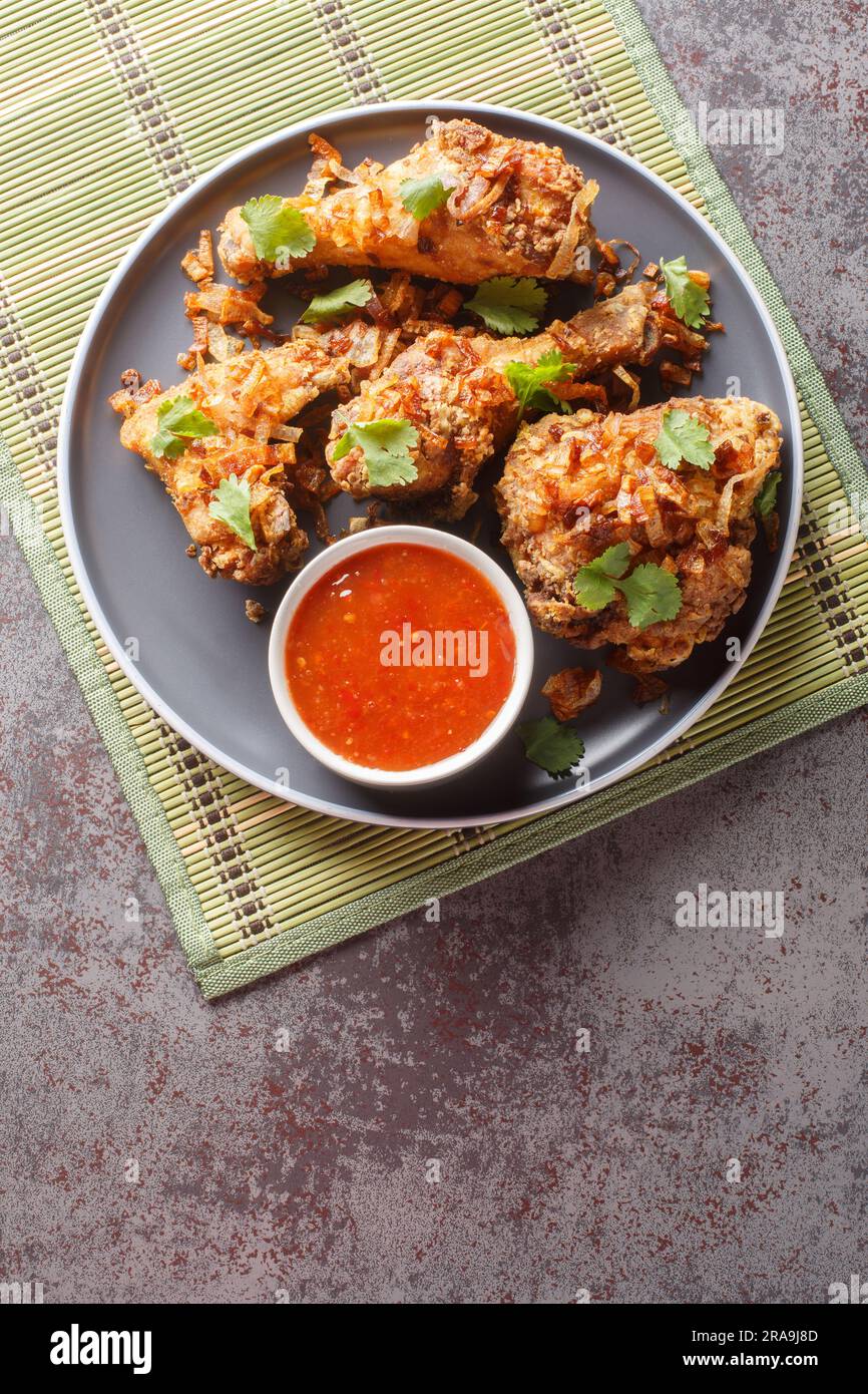 Hachez le poulet frit thaï de style Yai avec un oignon croustillant en gros plan sur une assiette sur la table. Vue verticale du dessus Banque D'Images