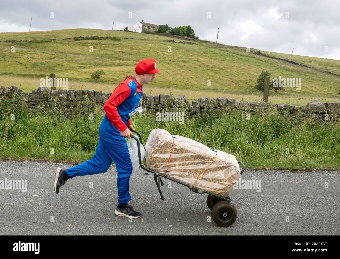 Un concurrent participe à la course de paille d'Oxenhope dans le West Yorkshire, une course de 2,5 miles en costume fantaisie tout en portant une balle de paille de 20kg le long de la route. Date de la photo: Dimanche 2 juillet 2023. La course a lieu chaque été dans le village Pennine d'Oxenhope, et a été lancé par deux hommes qui avaient un pari sur qui pourrait gagner une course d'un pub à l'autre portant une balle de paille. Le crédit photo devrait se lire comme suit : Danny Lawson/PA Wire Banque D'Images