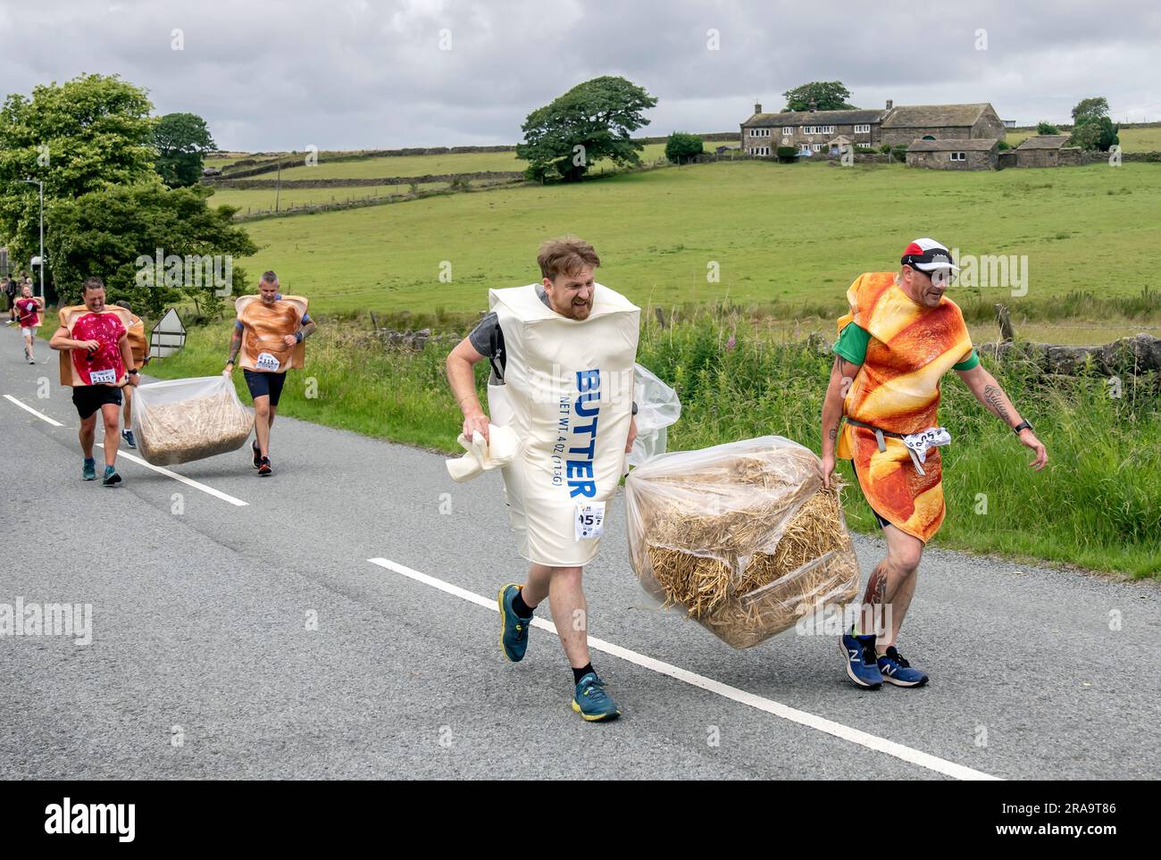 Les concurrents prennent part à la course de paille d'Oxenhope dans le West Yorkshire, une course de 2,5 kilomètres en costume fantaisie tout en portant une balle de paille de 20kg sur le trajet. Date de la photo: Dimanche 2 juillet 2023. La course a lieu chaque été dans le village Pennine d'Oxenhope, et a été lancé par deux hommes qui avaient un pari sur qui pourrait gagner une course d'un pub à l'autre portant une balle de paille. Le crédit photo devrait se lire comme suit : Danny Lawson/PA Wire Banque D'Images