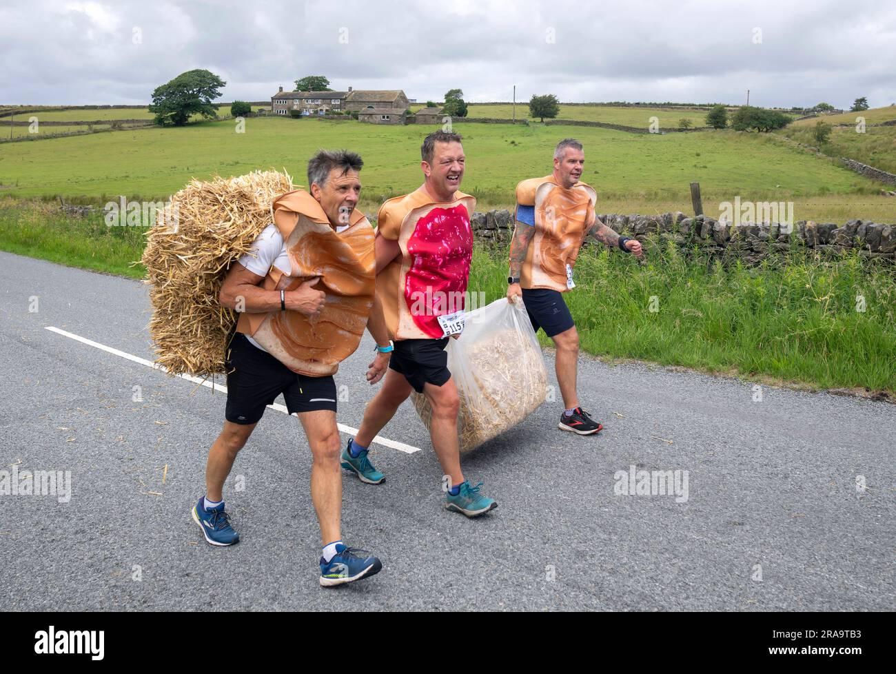 Les concurrents prennent part à la course de paille d'Oxenhope dans le West Yorkshire, une course de 2,5 kilomètres en costume fantaisie tout en portant une balle de paille de 20kg sur le trajet. Date de la photo: Dimanche 2 juillet 2023. La course a lieu chaque été dans le village Pennine d'Oxenhope, et a été lancé par deux hommes qui avaient un pari sur qui pourrait gagner une course d'un pub à l'autre portant une balle de paille. Le crédit photo devrait se lire comme suit : Danny Lawson/PA Wire Banque D'Images