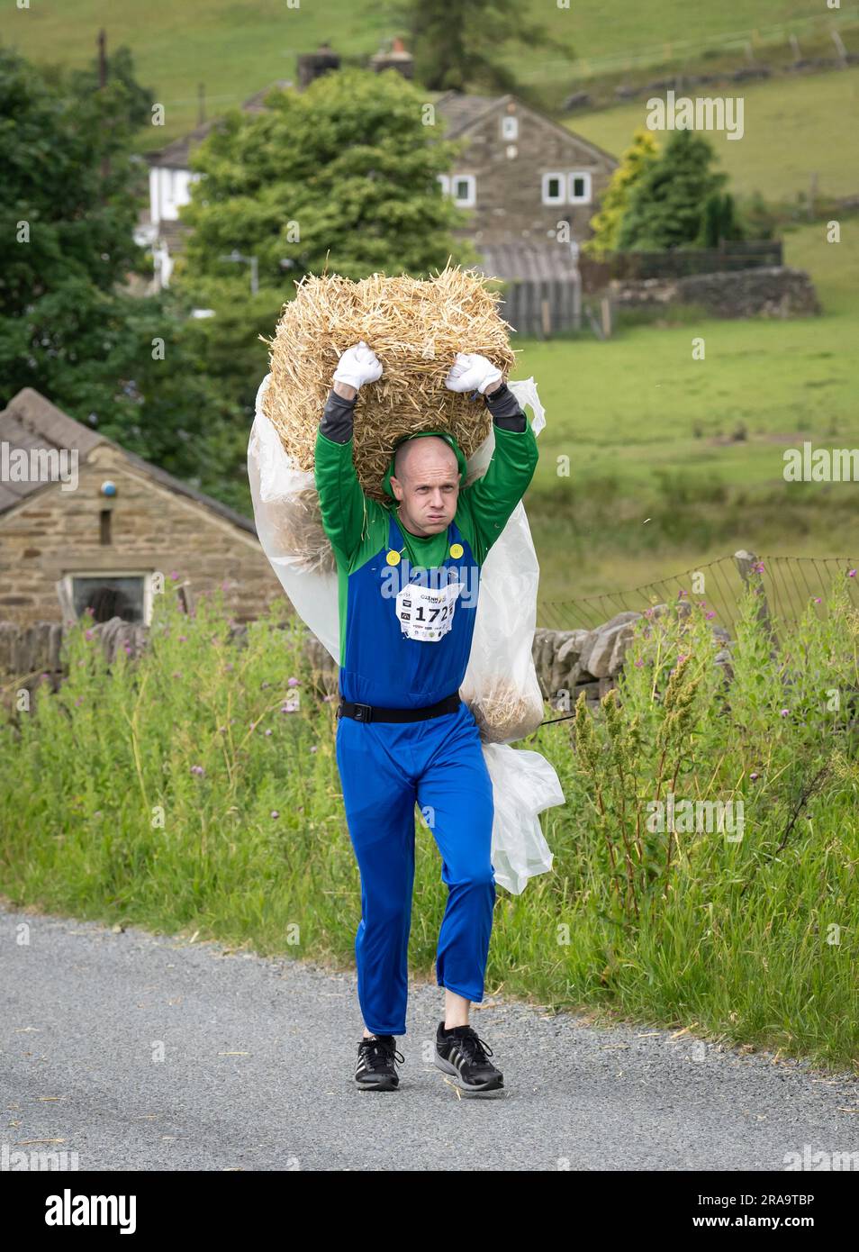 Un concurrent participe à la course de paille d'Oxenhope dans le West Yorkshire, une course de 2,5 miles en costume fantaisie tout en portant une balle de paille de 20kg le long de la route. Date de la photo: Dimanche 2 juillet 2023. La course a lieu chaque été dans le village Pennine d'Oxenhope, et a été lancé par deux hommes qui avaient un pari sur qui pourrait gagner une course d'un pub à l'autre portant une balle de paille. Le crédit photo devrait se lire comme suit : Danny Lawson/PA Wire Banque D'Images