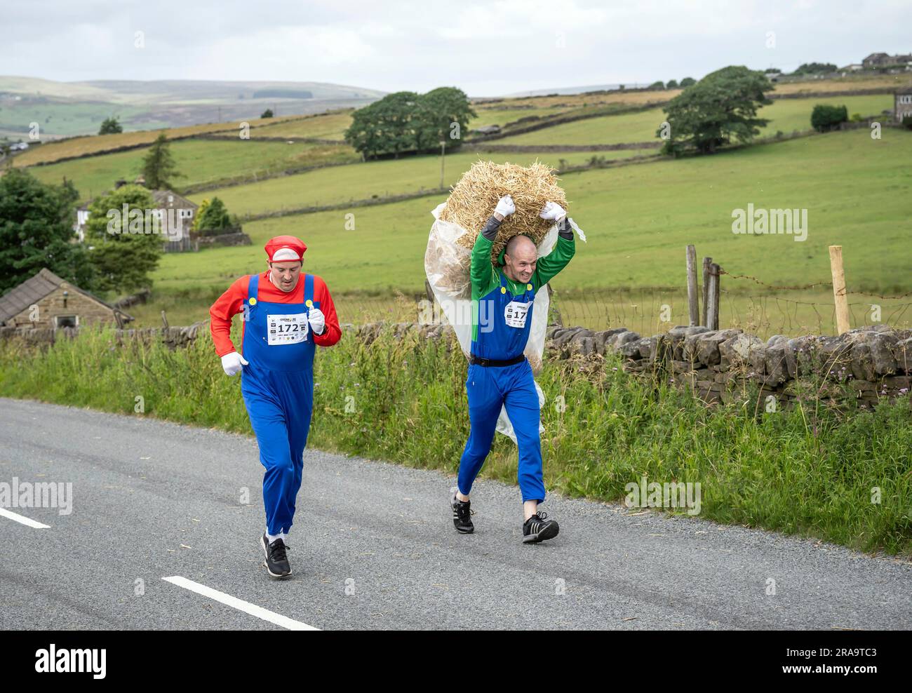 Les concurrents prennent part à la course de paille d'Oxenhope dans le West Yorkshire, une course de 2,5 kilomètres en costume fantaisie tout en portant une balle de paille de 20kg sur le trajet. Date de la photo: Dimanche 2 juillet 2023. La course a lieu chaque été dans le village Pennine d'Oxenhope, et a été lancé par deux hommes qui avaient un pari sur qui pourrait gagner une course d'un pub à l'autre portant une balle de paille. Le crédit photo devrait se lire comme suit : Danny Lawson/PA Wire Banque D'Images
