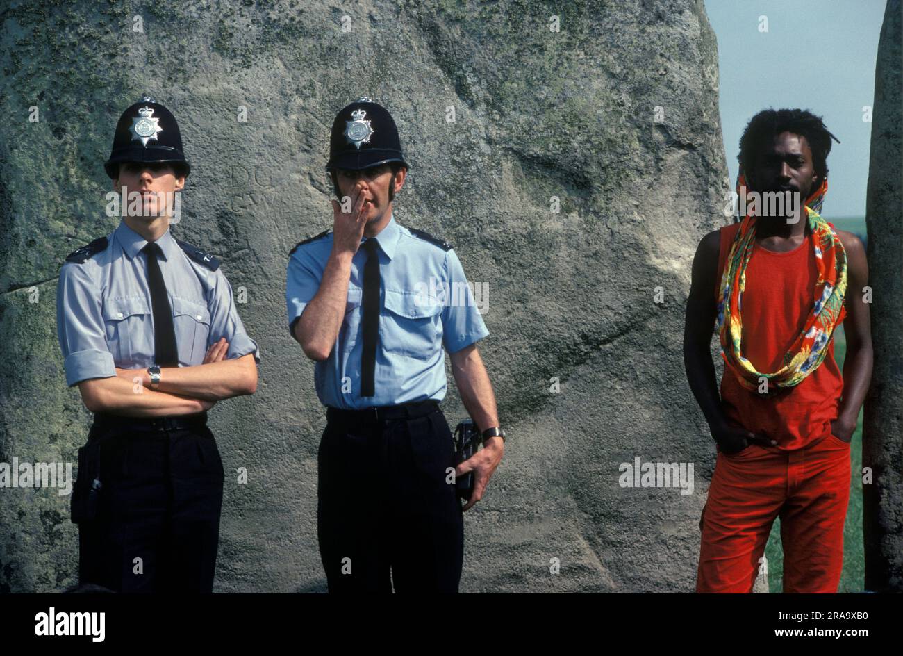 Policier sous la couverture. Stonehenge Free Festival au solstice d'été, Wiltshire, Angleterre 21 juin 1979. Deux policiers dans des manches de chemise et à l'aspect informel. On murmure d'une main en travers de sa bouche, à un policier britannique noir qui tente de ne pas paraître visible ! 1970S ROYAUME-UNI HOMER SYKES Banque D'Images