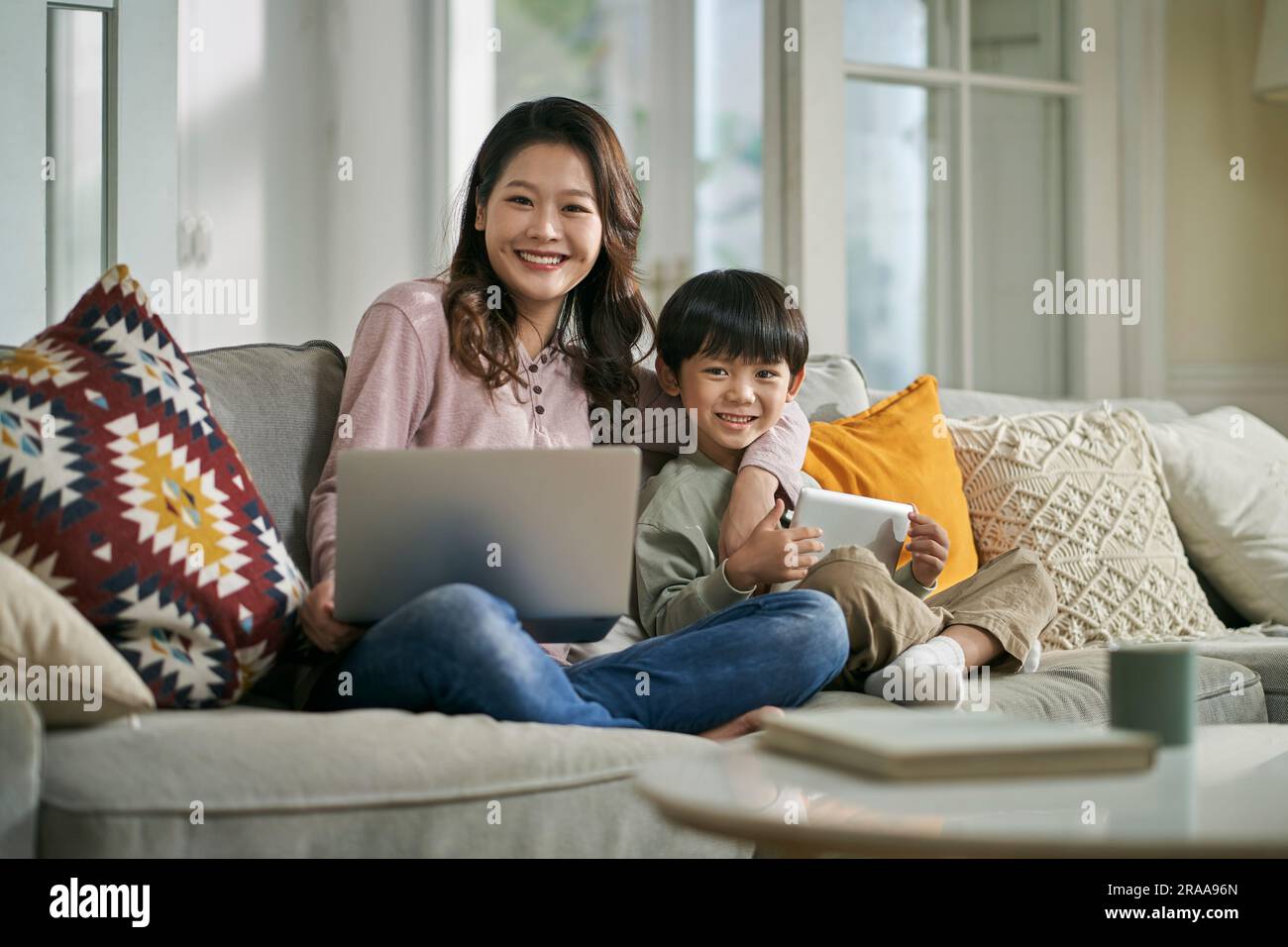 belle mère asiatique et fils de cinq ans assis sur un canapé de famille à la maison en regardant la caméra sourire Banque D'Images