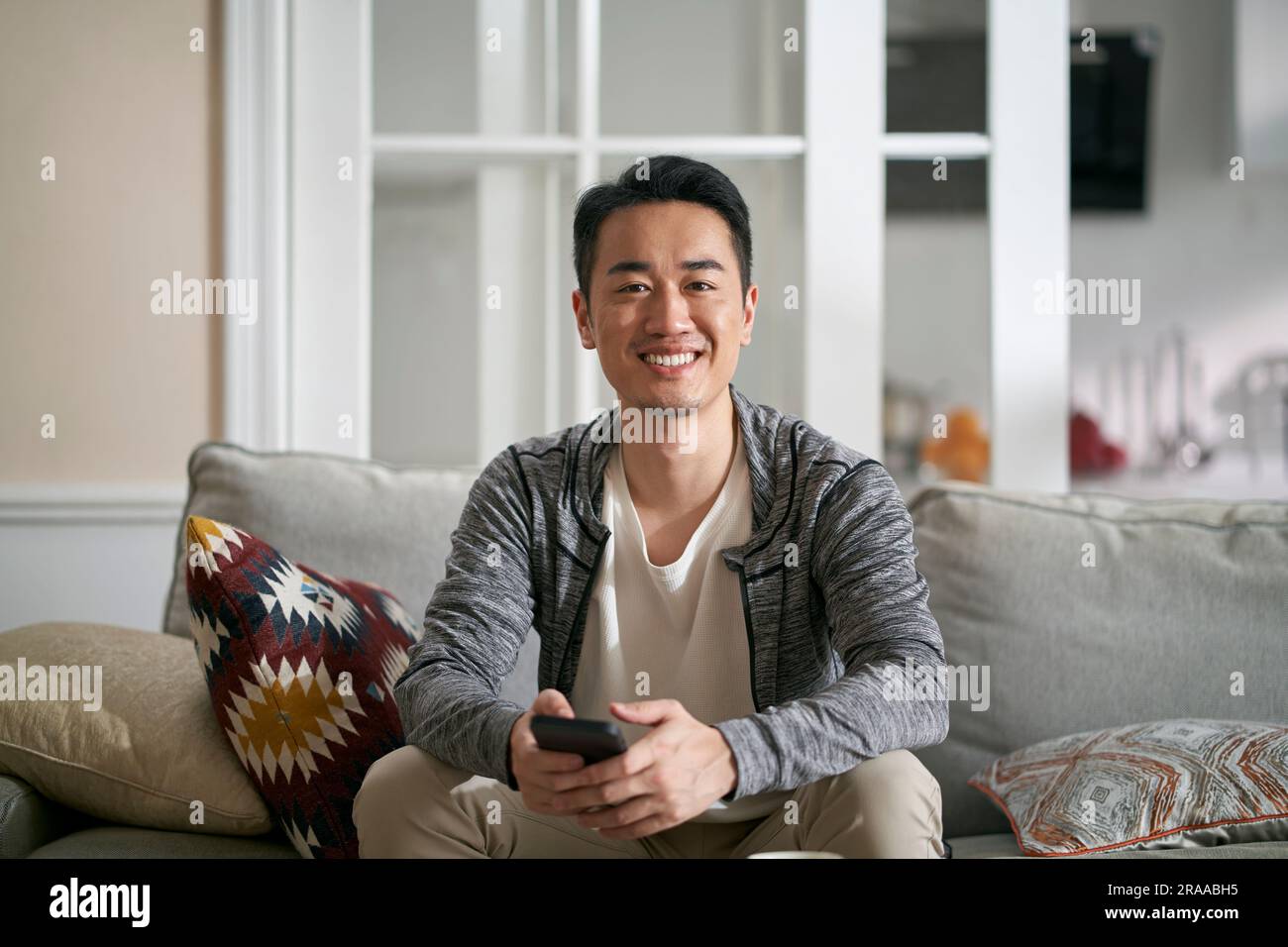 portrait d'un jeune homme asiatique heureux assis sur un canapé de famille en regardant l'appareil-photo sourire Banque D'Images