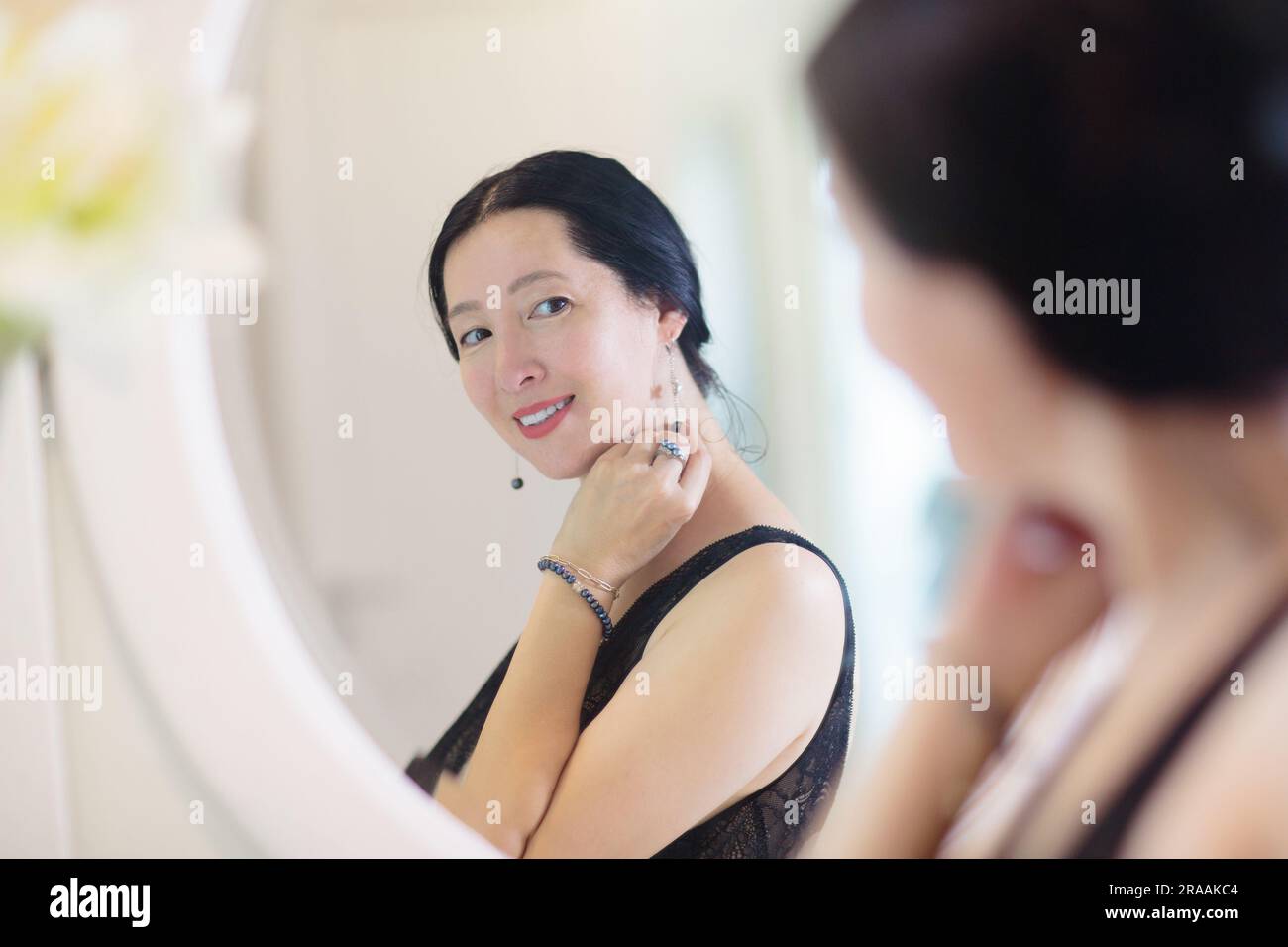 Jeune femme asiatique regardant dans le miroir. Soin de la peau. Belle femme dans une robe de nuit appliquant de la crème le jour le soir ou le week-end matin. Banque D'Images