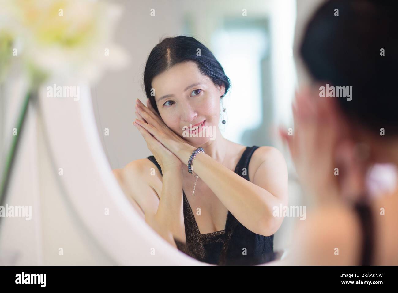 Jeune femme asiatique regardant dans le miroir. Soin de la peau. Belle femme dans une robe de nuit appliquant de la crème le jour le soir ou le week-end matin. Banque D'Images