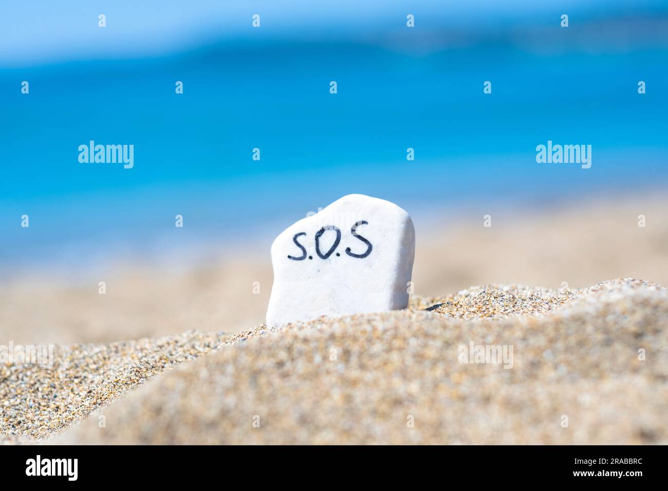 SOS - le mot dessin sur une pierre dans le sable sur la plage sur le fond de turquoise de la mer. Aide. Sauvez l'océan. Écologie et environnement Banque D'Images