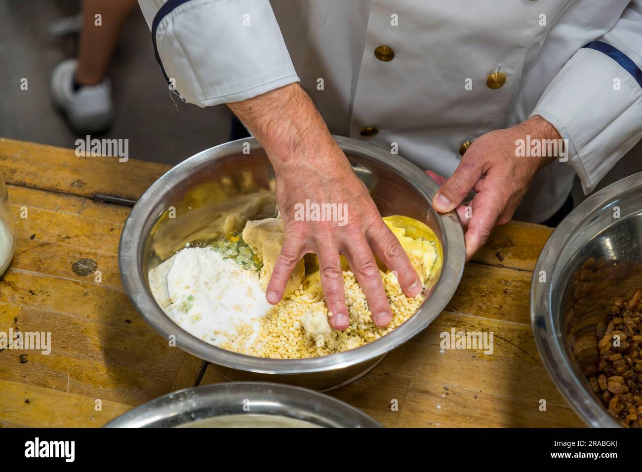 Un boulanger en veste de chef mélange de la farine, du sucre, des amandes hachées et de la pâte d'amandes dans un bol en métal pour le Christstollen d'origine de Dresde. Le sucre, les amandes, le beurre et les zestes candis de citron et d'orange sont combinés en un mélange de base. La photographie a été prise à la boulangerie Dresdner Backhaus, Dresde, Saxe, Allemagne. Banque D'Images