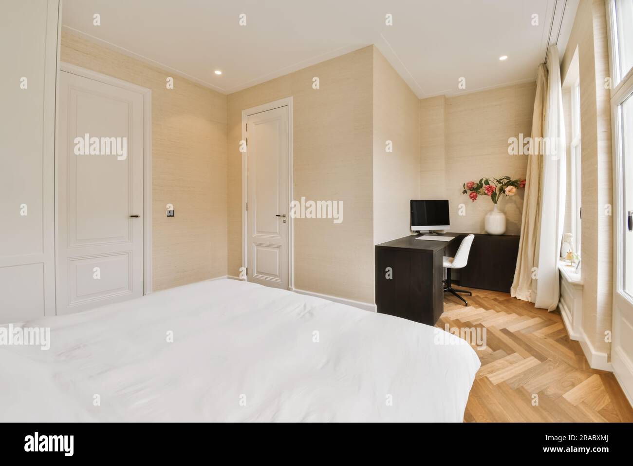 une chambre avec parquet et draps blancs sur le lit, il y a un petit bureau en face de la fenêtre Banque D'Images