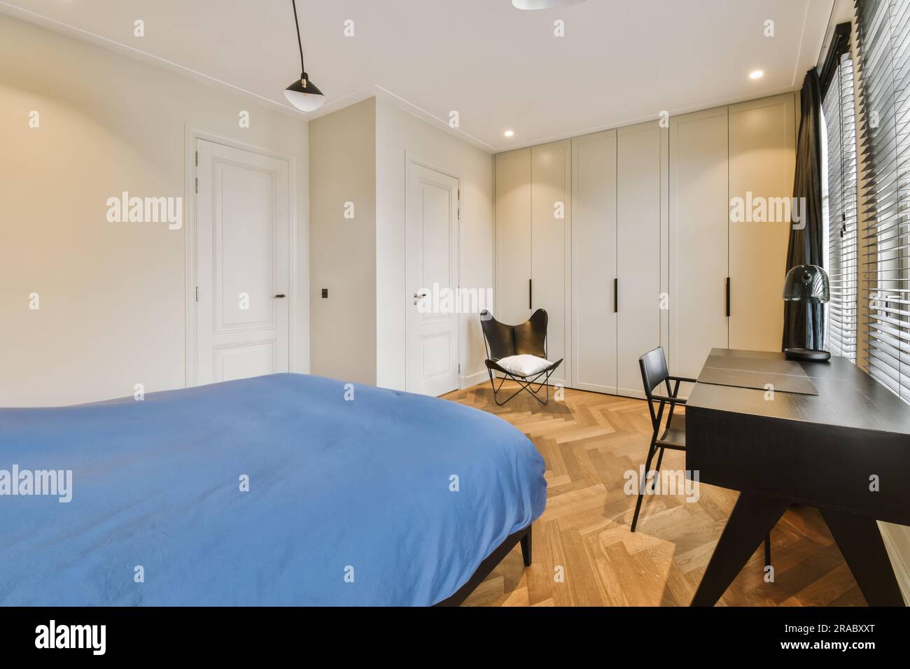 une chambre avec des placards blancs et des draps bleus sur le lit en face du lit est une chaise noire Banque D'Images
