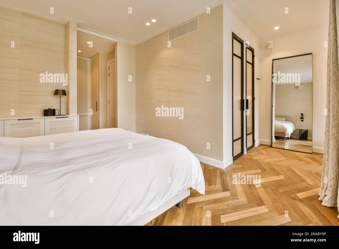 une chambre avec parquet et draps blancs sur le lit, devant un miroir qui est suspendu au-dessus Banque D'Images