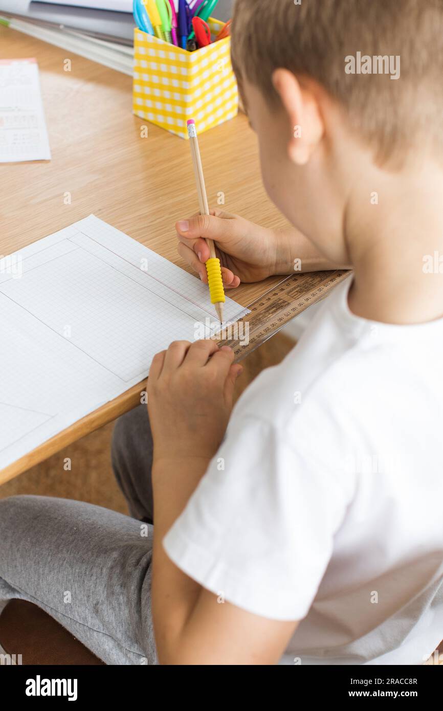 Un joli garçon fait un dessin avec une règle et un crayon. Leçons à la maison. Géométrie et dessin. Banque D'Images
