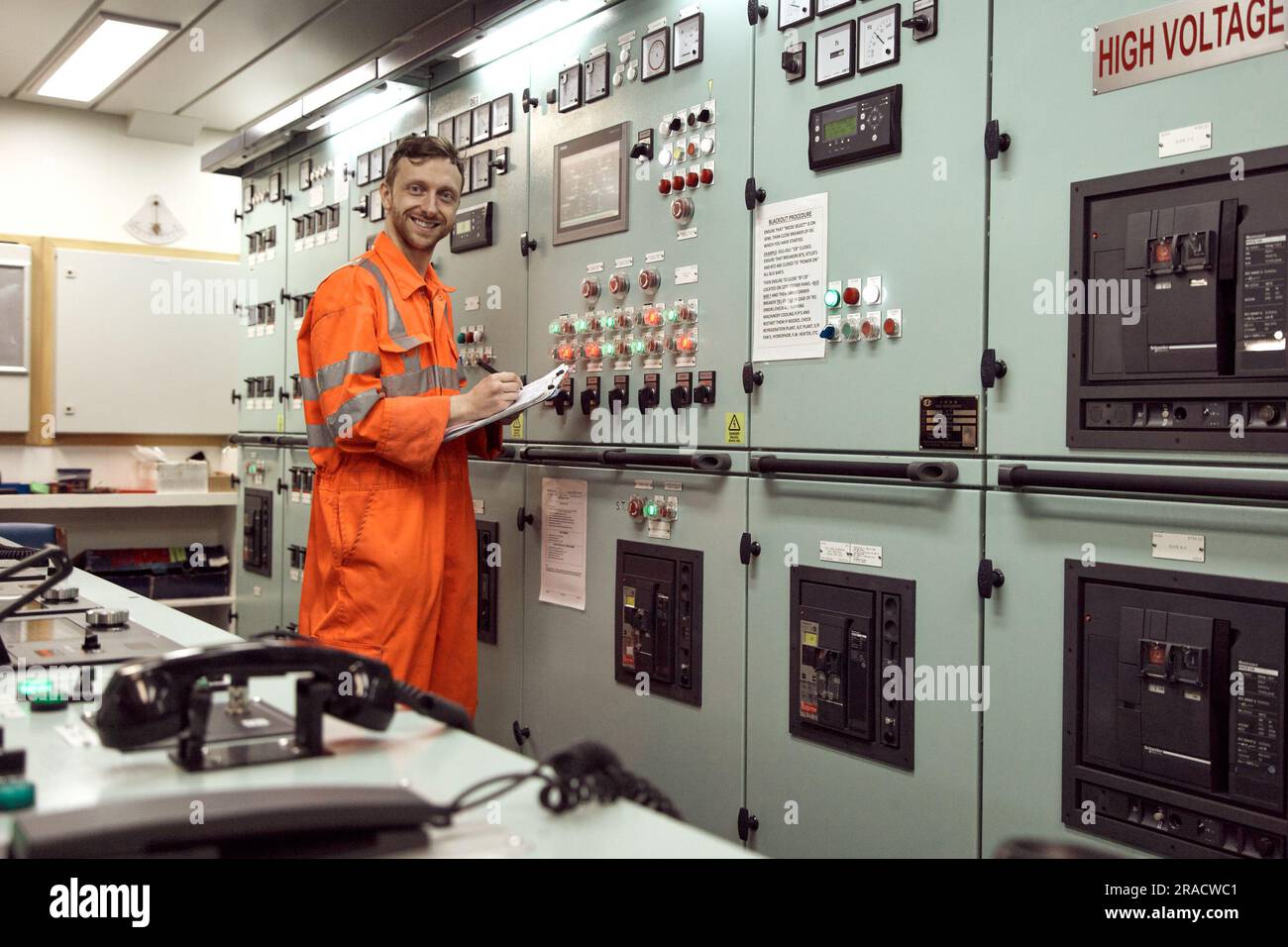 Jeune ingénieur mécanicien prenant des mesures de l'équipement de contrôle. Jeune technicien offshore souriant. Banque D'Images