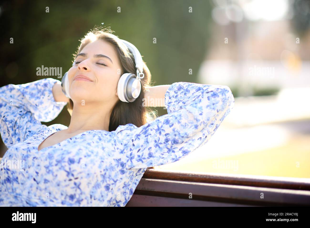 Une femme heureuse écoutant de la musique se reposant sur un banc dans un parc Banque D'Images
