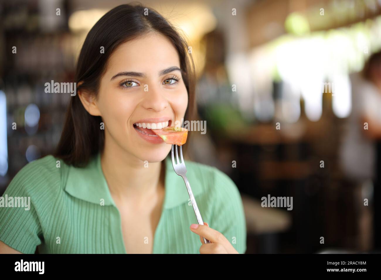 Un client satisfait du restaurant qui mange de la tomate en regardant un appareil photo Banque D'Images