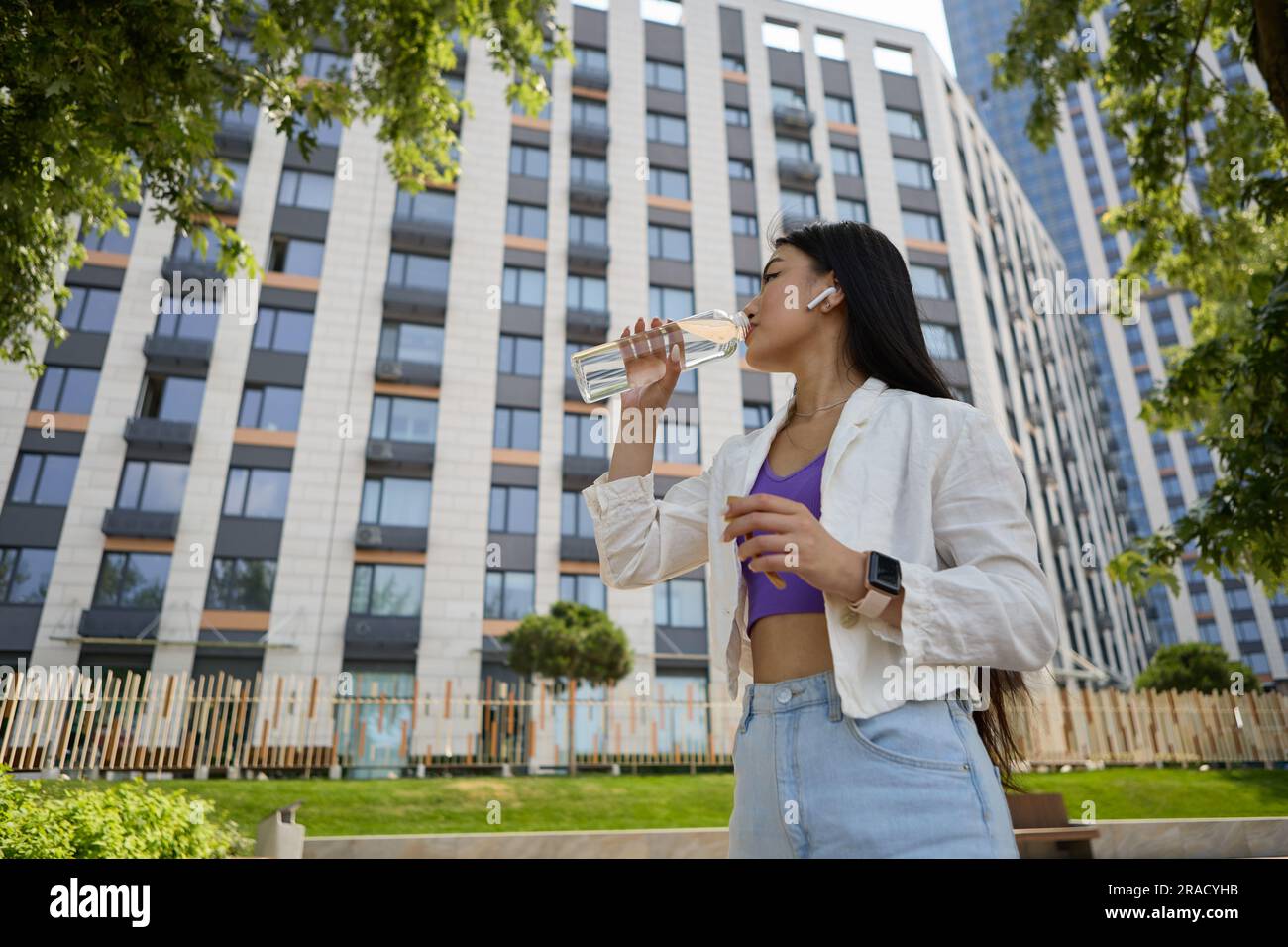 Belle jeune femme vietnamienne boit de l'eau minérale à partir d'une bouteille de verre lors d'une promenade. Portrait d'une jolie femme d'Asie du Sud-est en 20s Banque D'Images