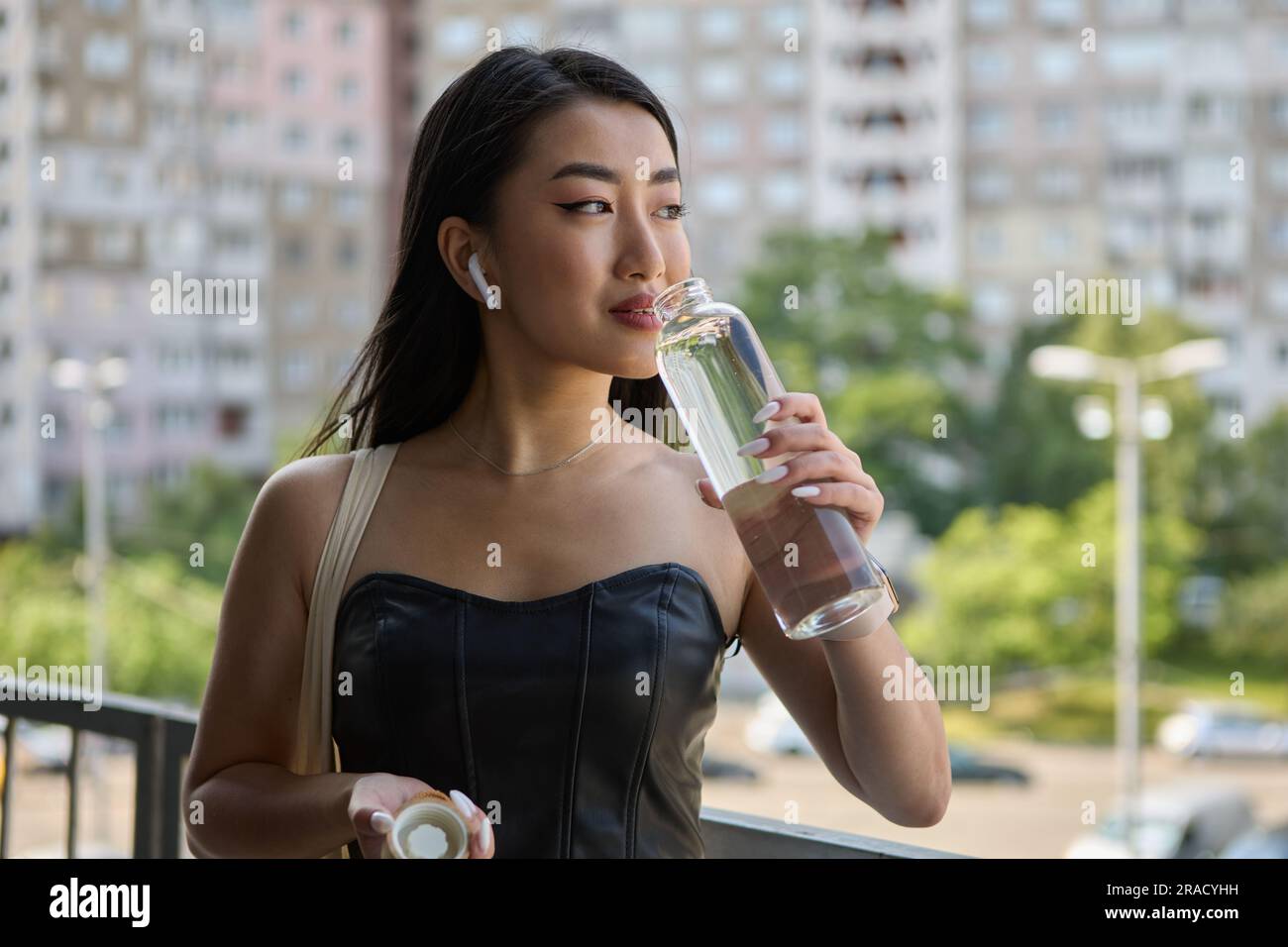 Portrait d'une belle jeune femme vietnamienne de l'eau potable d'une bouteille de verre. Une femme assoiffée prend une gorgée d'eau minérale avec un sourire Banque D'Images
