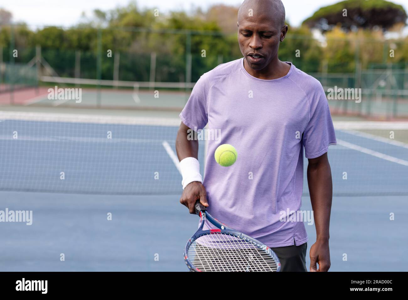 Joueur de tennis masculin afro-américain concentré rebondissant balle sur raquette sur un court extérieur Banque D'Images