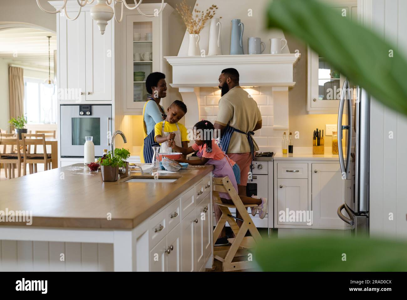 Frères et sœurs afro-américains mélangeant la pâte dans un bol sur un îlot de cuisine avec des parents en arrière-plan à la maison Banque D'Images