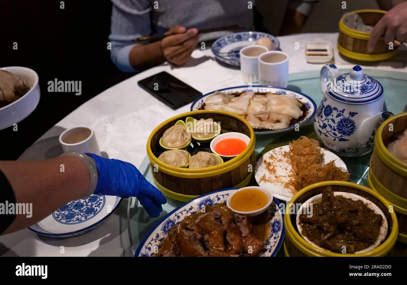 Femme main avec gant tournant table ronde plein de plats Yumcha. Smartphone sur la table. Banque D'Images