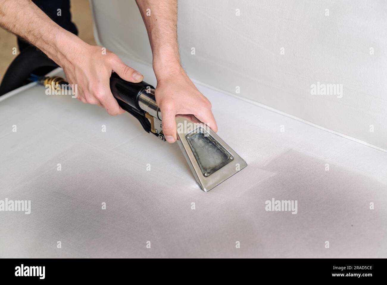 Gros plan de la femme de ménage tenant l'aspirateur de lavage moderne et le nettoyage du canapé sale avec une tache avec un détergent professionnel. Banque D'Images