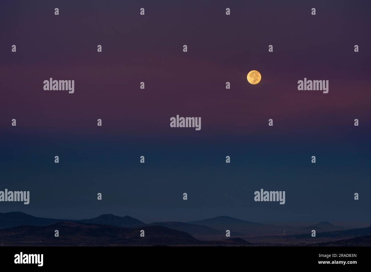 Pleine lune juste avant de se cacher à l'horizon avec un ciel violet Banque D'Images