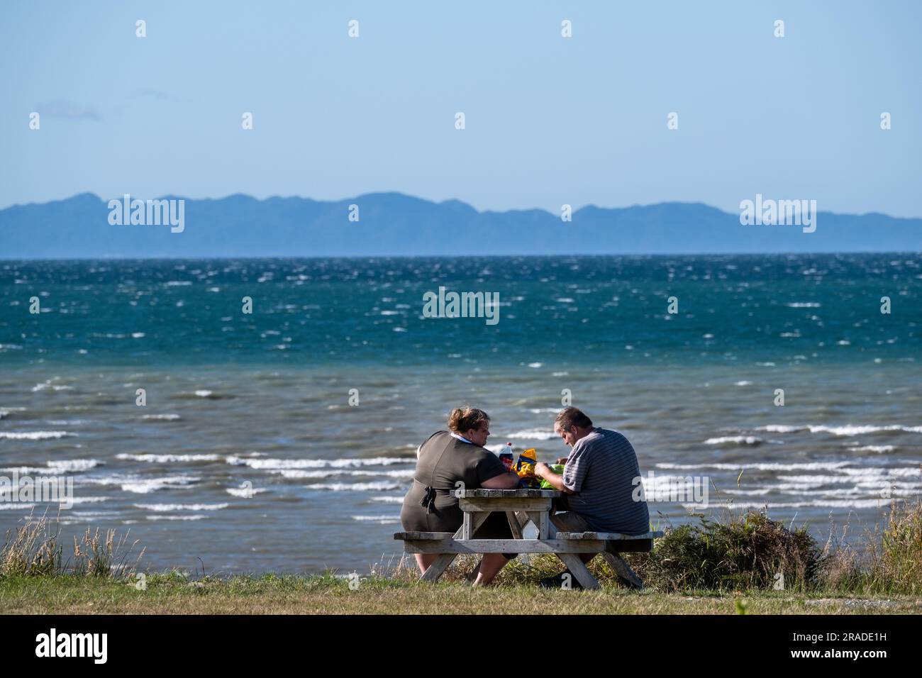 Un couple obèse partage un pique-nique sur la plage dans la région côtière de Takaka sur Golden Bay près du parc national Abel Tasman sur l'île du Sud, en Nouvelle-Zélande. Banque D'Images