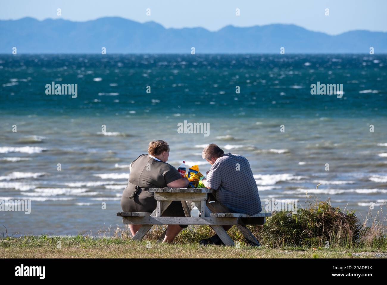 Un couple obèse partage un pique-nique sur la plage dans la région côtière de Takaka sur Golden Bay près du parc national Abel Tasman sur l'île du Sud, en Nouvelle-Zélande. Banque D'Images